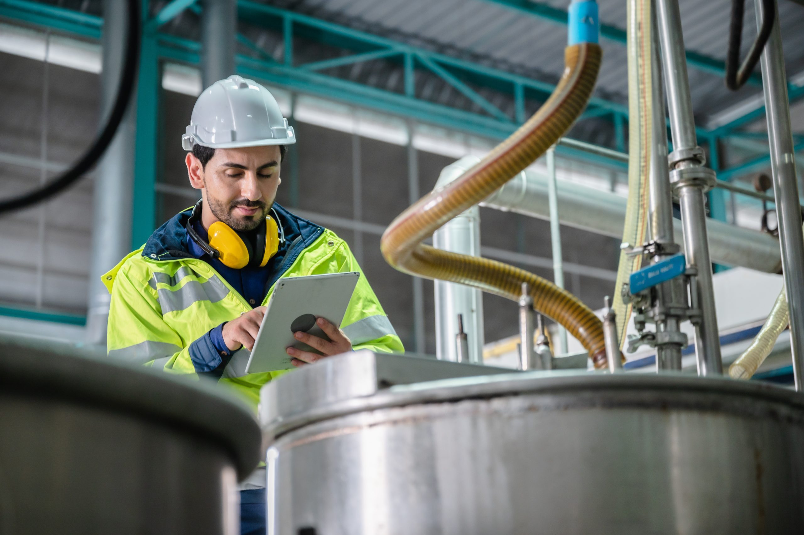 A man in a hard hat checks a tablet at a beverage manufacturing facility